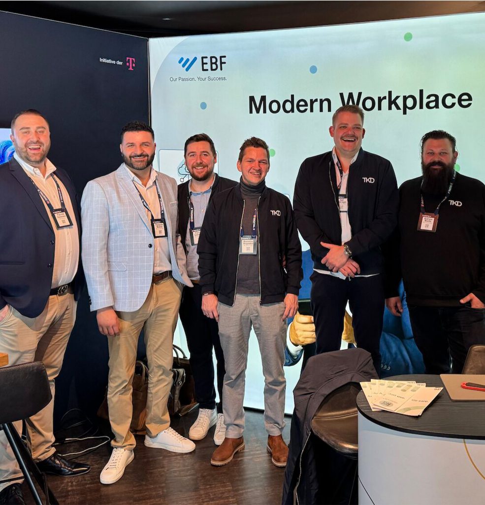 Mehrere Personen des Vertriebteams sind zu sehen vor unserer Messewand an unserem Messestand auf der Regiodigital X. Alle lächeln und stehen in einer Reihe.